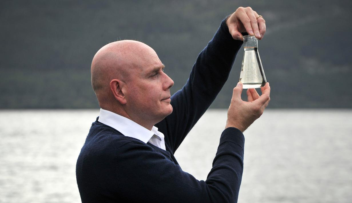 Ahli genetika Universitas Otago Profesor Neil Gemmell berpose dengan wadah air di perairan Loch Ness, Drumnadrochit, Skotlandia, Kamis (5/9/2019). Para ilmuwan mencoba mengurai keberadaan monster legendaris asal Inggris, Loch Ness. (Andy Buchanan/AFP)