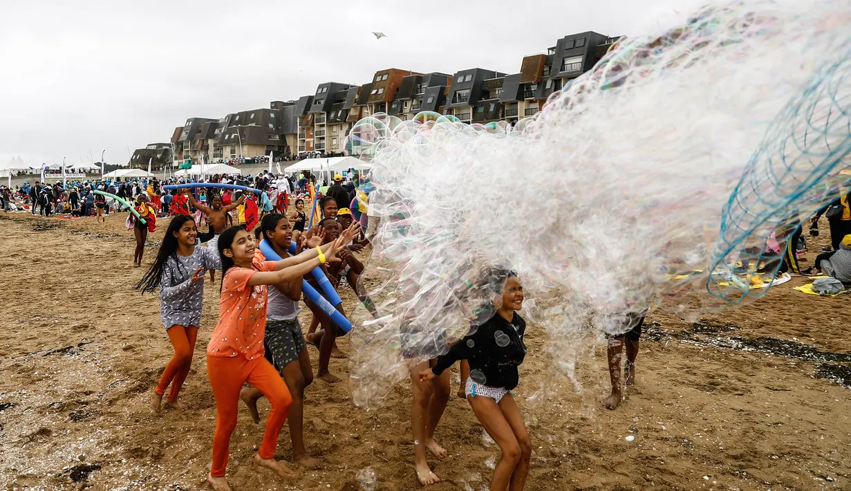 Anak-anak bermain dengan gelembung di pantai Cabourg, barat laut Prancis (18/8/2021). Seratus bus meninggalkan wilayah Paris dari delapan departemen Ile-de-France dengan 5.000 anak muda dari Ile-de-France dalam situasi genting yang belum sempat berangkat musim panas ini. (AFP/Sameer Al-Doumy)