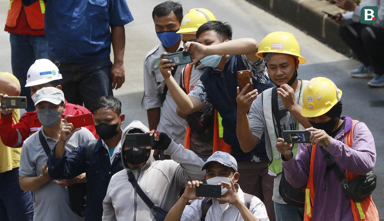 Para pekerja proyek mengabadikan momen parade pembalap MotoGP di depan Sarinah Thamrin, Jakarta Pusat. Sebanyak 20 pembalap melakukan parade motor dari Istana Merdeka menuju Hotel Kempinski di Bundaran HI Jakarta Pusat, Rabu (16/03/2022). (Bola.com/M Iqbal Ichsan)