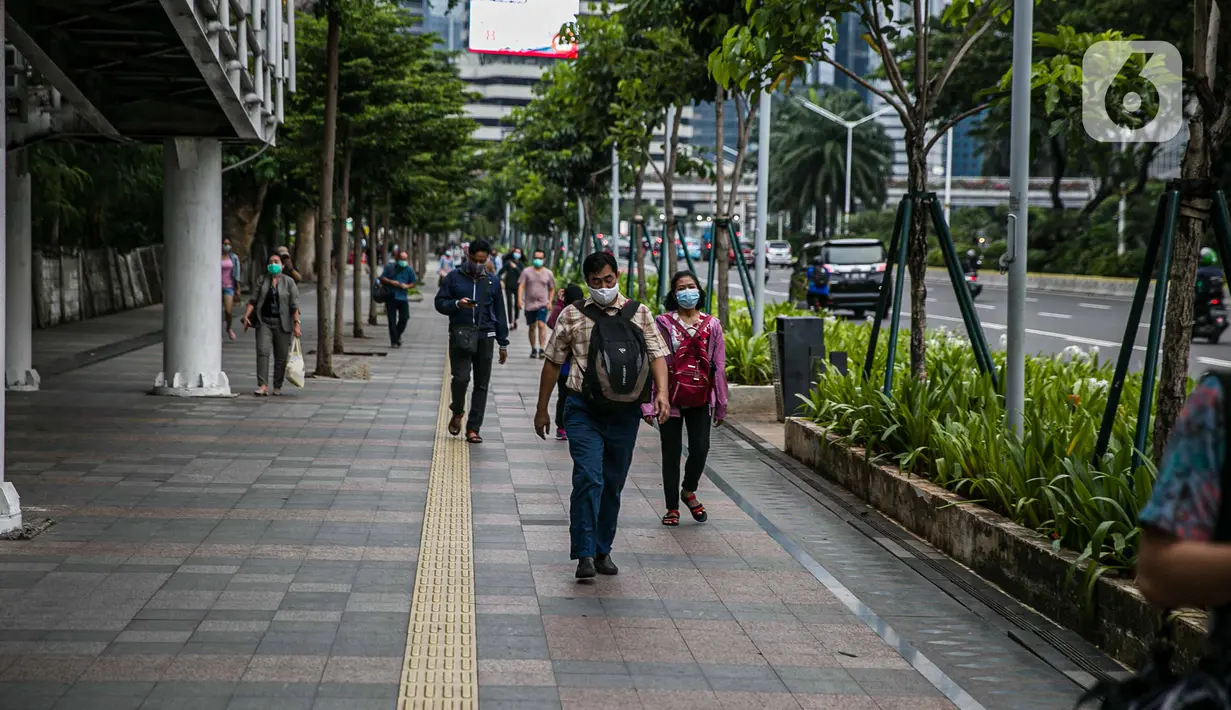 Pekerja kantoran berjalan di trotoar Jalan Sudirman, Jakarta Pusat, Rabu (6/1/2021). Selama pembatasan sosial berskala besar (PSBB) di wilayah Jawa dan Bali pada 11-25 Januari 2021, aktivitas bekerja di kantor diperketat dengan sistem work from home (WFH) 75 persen. (Liputan6.com/Faizal Fanani)