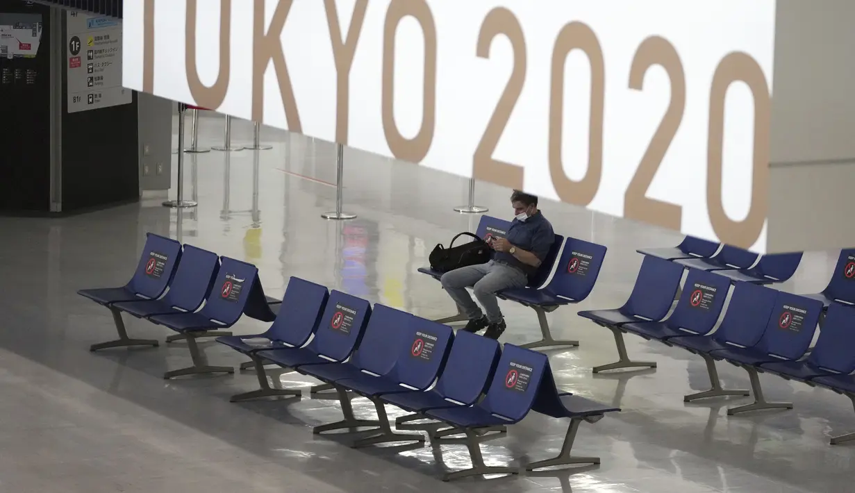 Sorang pria yang mengenakan masker pelindung untuk membantu mengekang penyebaran virus corona berhenti di dekat spanduk Olimpiade Tokyo 2020 di Bandara Internasional Narita, Tokyo, Selasa siang (1/6/2021). (AP Photo/Eugene Hoshiko)
