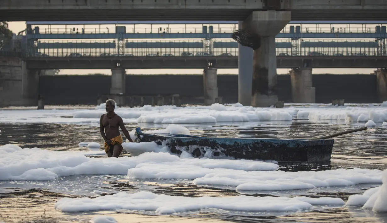 Seorang pria menarik perahu di tengah busa di sungai Yamuna yang tercemar di pinggiran New Delhi (23/7/2020). Sungai yang sangat dianggap suci oleh umat Hindu India ini masih tercemar, salah satunya akibat busa polusi memenuhinya. (AFP Photo/Xavier Galiana)