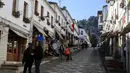 Dua gadis berdiri di luar toko saat pekerja membersihkan jalan di kota Gjirokastra, Albania pada 5 Februari 2021. Pariwisata telah berkembang di kota Gjirokastra, yang diakui sebagai Situs Warisan Dunia UNESCO, tetapi pandemi virus corona menghentikannya secara tiba-tiba. (AP Photo/Hektor Pustina)