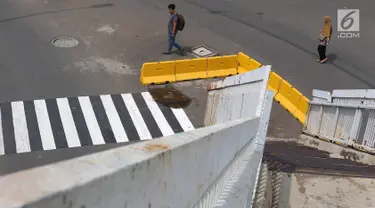 Pejalan kaki melintas di dekat tangga JPO yang berada di tengah jalan Dewi Sartika, Jakarta, Rabu (9/1). Adanya proyek pelebaran jalan menyebabkan posisi trotoar bergeser sehingga tangga JPO menjadi di tengah jalan. (Liputan6.com/Immanuel Antonius)