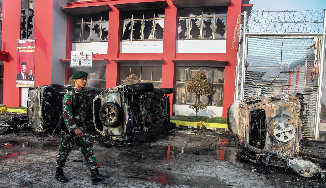 Petugas melintasi dampak kerusuhan di Lapas Narkotika Kelas III Langkat, Sumatera Utara, Kamis (16/5/2019). Akibat peristiwa kerusuhan yang dilakukan para narapidana di Lapas itu mengakibatkan tiga mobil dan dua sepeda motor petugas rusak terbakar dan ratusan napi melarikan diri. (Ivan Damanik/AFP)
