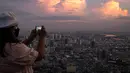 Seorang wanita mengambil foto cakrawala dari dek observasi pencakar langit King Power Mahanakhon saat matahari terbenam di Bangkok, Thailand pada 25 Oktober 2021. Gedung yang dibuka pada tahun 2017 lalu ini memiliki 77 lantai dengan tinggi 324 meter. (Jack TAYLOR / AFP)