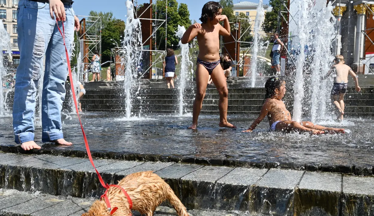 Anak-anak bermain di air mancur dii Independence Square di Kiev selama gelombang panas di ibukota Ukraina (21/8/2019). Panasnya cuaca yang ekstrem membuat anak-anak menyejukkan diri mereka di bawah guyuran air mancur. (AFP Photo/Sergei Supinsky)