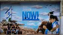 Orang-orang duduk di samping grafiti yang menyerukan kembalinya para sandera yang diculik dalam serangan lintas batas Hamas pada 7 Oktober di Israel, di luar pemakaman di Kfar Saba, Israel, Minggu, 12 November 2023. (AP Photo/Ariel Schalit)