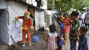 Relawan pekerja sosial, Ashok Kurmi berinteraksi dengan anak-anak saat mendisinfeksi ruang publik di daerah kumuh Mumbai pada 2 Juni 2021. Kurmi turun tangan memerangi virus Corona COVID-19 di daerah kumuh Mumbai menggunakan aksesori yang tidak biasa, yaitu kostum badut. (INDRANIL MUKHERJEE/AFP)