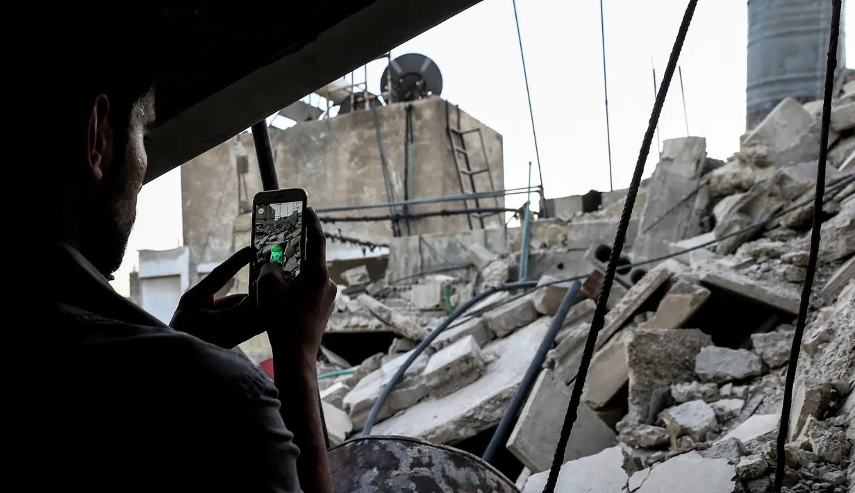 Seorang gamer Suriah menggunakan aplikasi Pokemon Go di ponselnya untuk mencari Pokemons di antara puing-puing di kota Douma, Damaskus (23/7). (AFP PHOTO / Sameer Al-Doumy)