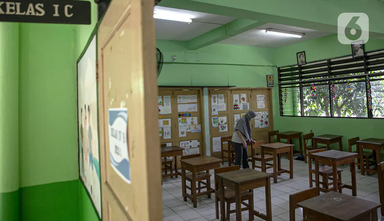Seorang guru membersihkan kelas yang akan digunakan di SDN Kenari 08, Jakarta, Selasa (6/4/2021). Uji coba pembelajaran tatap muka terbatas di DKI Jakarta akan dilakukan dengan menerapkan protokol kesehatan COVID-19 yang ketat. (Liputan6.com/Faizal Fanani)