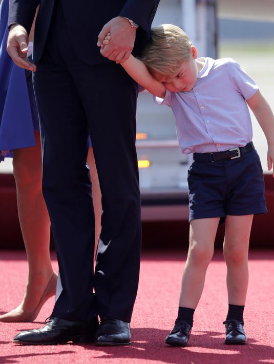 Pangeran George menyenderkan kepalanya ke tangan ayahnya, Pangeran William sesampainya di bandara Tegel, Berlin, Rabu (19/7). Ikut dalam tur keluarga kerajaan Inggris, George kelihatan lelah dan mengantuk saat turun pesawat. (Kay Nietfeld/POOL/AFP)