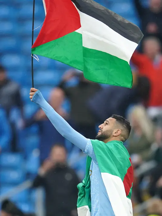 Gelandang Manchester City, Riyad Mahrez mengibarkan bendera Palestina saat merayakan timnya meraih gelar Liga Inggris di stadion Etihad, Minggu (23/5/2021). Pada 10 Mei lalu, Mahrez memposting foto bendera Palestina di akun media sosialnya. (AFP Photo/Pool/Dave Thompson)