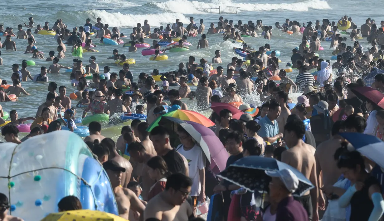 Orang-orang mendinginkan diri sambil bermain di sebuah pantai di Qingdao, China timur, pada 3 Agustus 2019. Banyak warga di Negeri Tirai Bambu memanfaatkan musim panas dengan mengunjungi pantai untuk mengisi liburan. (Photo by FRED DUFOUR / AFP)