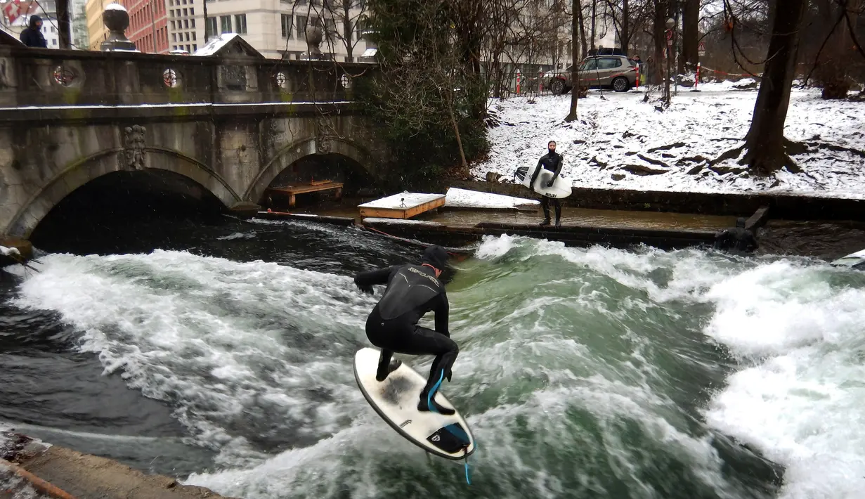 Aksi peselancar menaklukkan ombak saat berselancar di Sungai Eisbach selama hari musim dingin di Munich, Jerman, 4 Januari 2017. Tidak hanya peselancar lokal namun turis pun tertantang untuk mencoba berselancar di sungai kota Munich.  (Mark RALSTON/AFP)