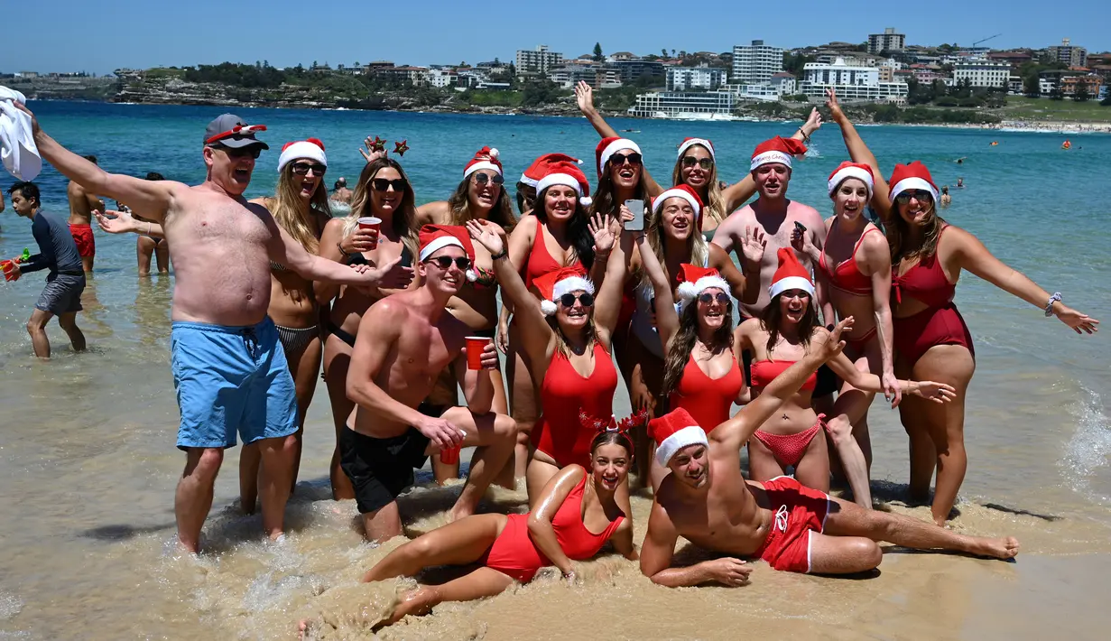 Sejumlah turis berpose mengenakan topi Santa di Pantai Bondi selama  Hari Natal 2018, Australia (25/12). (AFP Photo/Peter Parks)