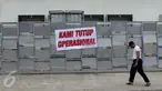 Warga melewati di spanduk 'Kami Tutup Operasional' di pabrik pengolahan ikan Pelabuhan Muara Baru, Jakarta, Senin (10/10). Mogok massal karena dibatasinya masa sewa di pelabuhan selama 5 tahun yang tadinya selama 20 tahun.  (Liputan6.com/Gempur M Surya)