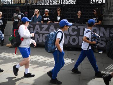 Anak-anak sekolah berjalan melewati aksi protes yang dilakukan oleh organisasi non-pemerintah Choose Love Europe di luar Gedung Parlemen di London, Inggris pada 29 Mei 2025. (Justin TALLIS/AFP)