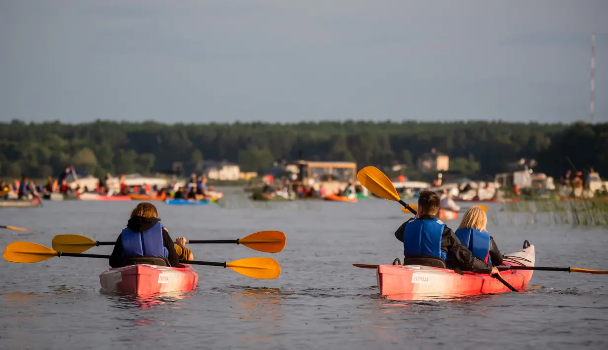 Para penonton mendayung perahu untuk menikmati konser musik Laivā di Danau Juglas, Riga, Latvia, 14 Agustus 2021. Hanya warga yang sudah divaksin COVID-19 yang diizinkan menonton konser dari darat. (Gints Ivuskans/AFP)