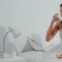 Seorang perempuan yang sedang sakit meminum segelas air putih (Foto Dok: Freepik/tirachardz).