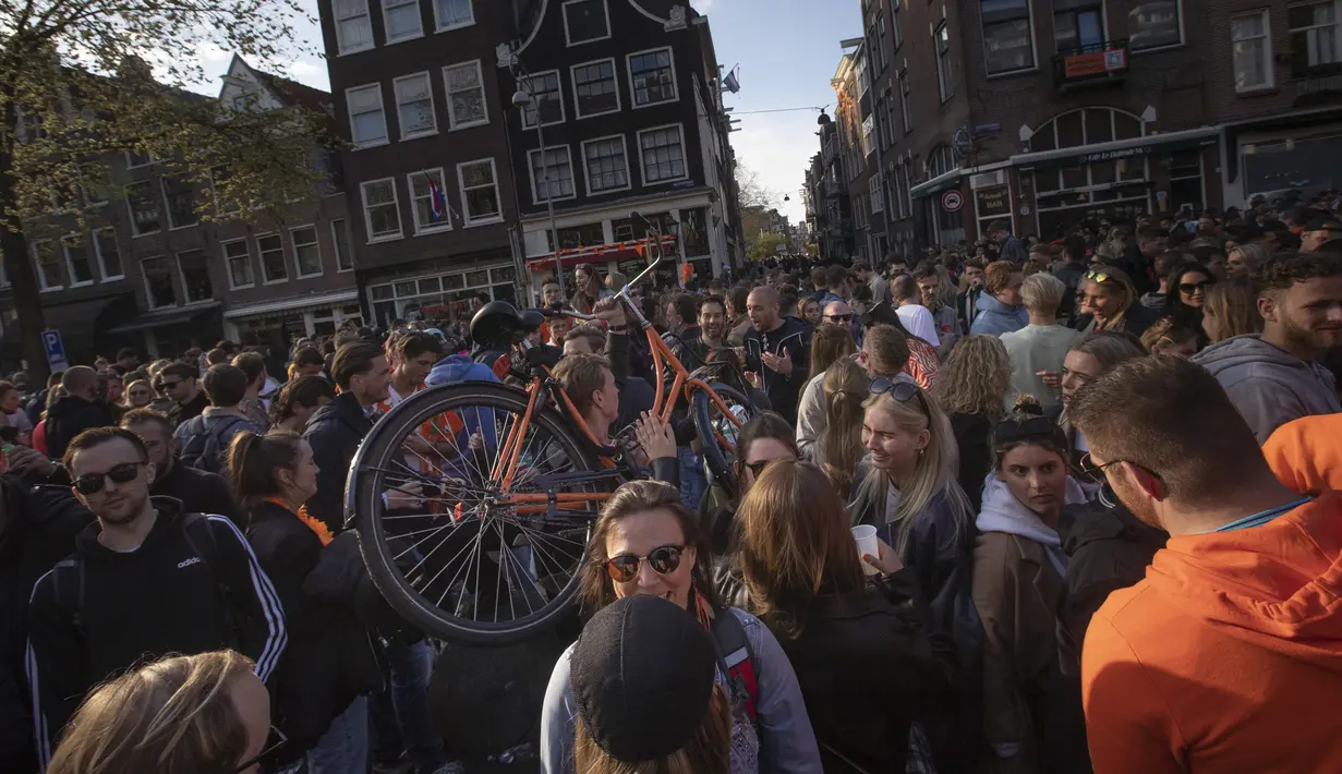 Seorang pria membawa sepedanya bergerak di antara kerumunan warga yang merayakan Hari Raja di pusat Kta Amsterdam, Belanda, Selasa (27/4/2021). Warga berkumpul di kota-kota seluruh Belanda untuk menandai ulang tahun Raja Willem-Alexander. (AP Photo/Peter Dejong)