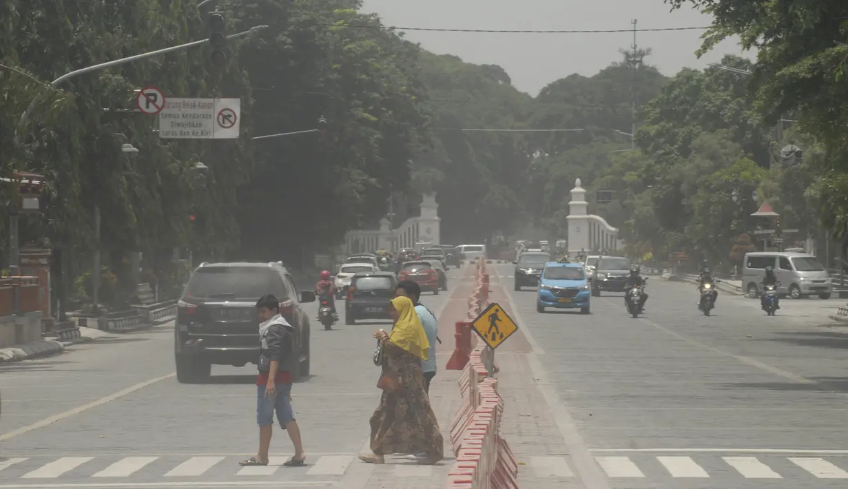 Orang-orang menyeberang jalan yang tertutup abu setelah letusan Gunung Merapi di Solo (3/3/2020). Gunung paling aktif di Indonesia tersebut meletus pada 3 Maret pukul 05.22 WIB dengan tinggi kolom 6.000 meter. (AFP Photo/Dika)