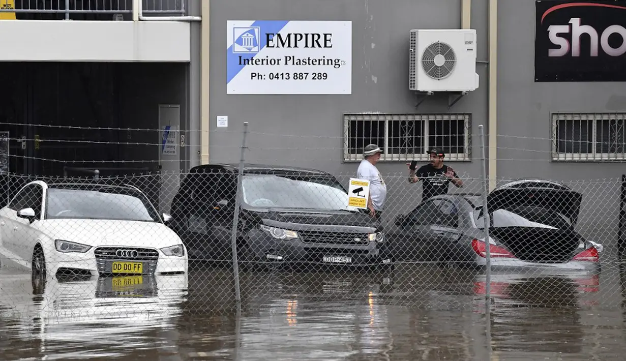 Staf Klub Olahraga Camden mengarungi banjir untuk masuk ke gedung di pinggiran barat daya Camden, Sydney, Australia, Selasa (8/3/2022). (Muhammad FAROOQ/AFP)