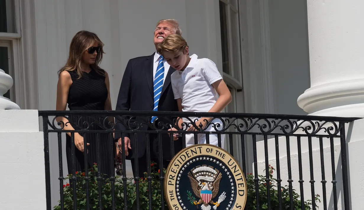 Presiden AS Donald Trump bersama Ibu Negara, Melania Trump dan putra mereka, Barron melihat gerhana matahari dari balkon Gedung Putih di Washington, Senin (21/8). Trump terlihat menyaksikan fenonema langka itu tanpa kacamata pelindung. (NICHOLAS KAMM/AFP)