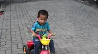 Tak ada orang dewasa yang menemani bocah tersebut. Dia asyik menggowes sepeda roda tiganya di Gang Bendungan Masjid. (Liputan6.com/Audrey Santoso)