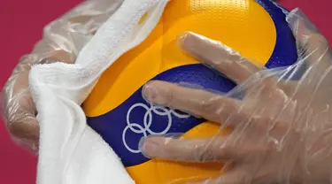 Petugas mengenakan sarung tangan plastik dan kain saat mendisinfeksi bola voli jelang pembukaan pertandingan voli Olimpiade Tokyo 2020 di Ariake Arena, Tokyo, Jepang, Jumat (23/7/2021). Olimpiade Tokyo 2020 digelar dengan penerapan protokol kesehatan ketat. (AP Photo/Frank Augstein)