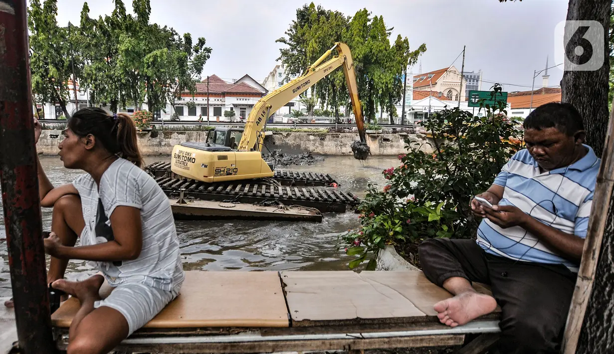Aktivitas warga di dekat kendaraan alat berat saat pengerukan lumpur Kali Pasar Baru, Jakarta, Minggu (23/5/2021). Pengerukan lumpur Kali Pasar Baru yang merupakan aliran Kali Ciliwung itu guna mencegah pendangkalan serta mengantisipasi banjir di musim penghujan. (merdeka.com/Iqbal S Nugroho)