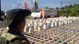 Foto yang dirilis kepolisian Kolombia terlihat petugas berdiri di dekat  8 ton paket kokain yang disita di sepanjang wilayah perbatasan dengan Panama, Minggu (15/5). Menurut pejabat setempat, ini adalah penemuan terbesar di Kolombia (Colombian Police/AFP)
