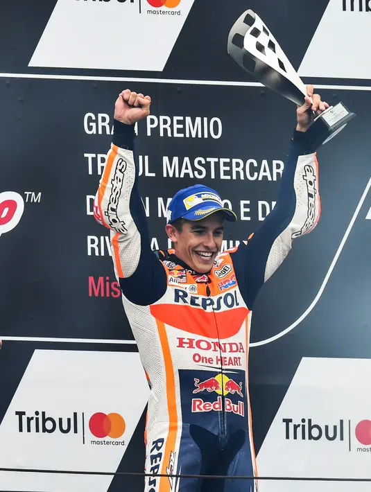 Pembalap Repsol Honda, Marc Marquez memegang trofi juara balapan MotoGP San Marino 2017 di atas podium, Minggu (10/9). Kemenangan Marquez cukup dramatis dengan menyalip pembalap Octo Pramac Ducati Danilo Petrucci di putaran terakhir. (ANDREAS SOLARO/AFP)