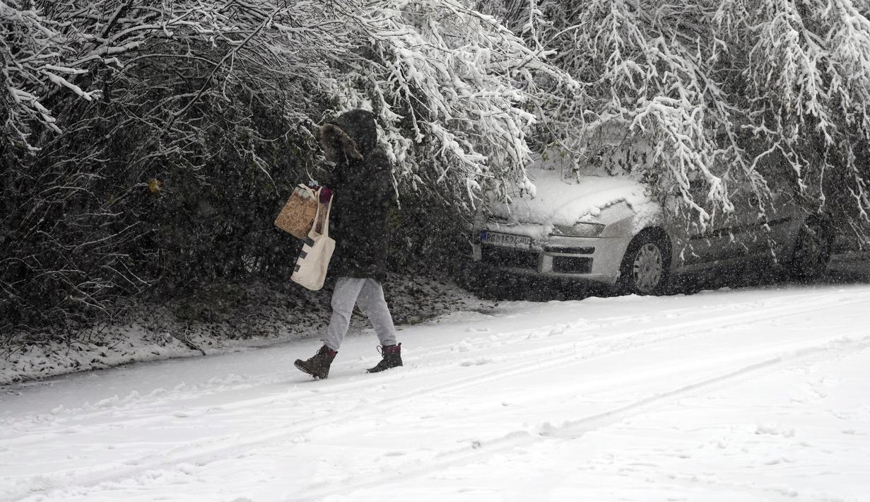 Seorang perempuan melintasi jalan yang tertutup salju di Beograd, Serbia, Minggu (12/12/2021). Ahli meteorologi memperkirakan hujan salju lebat dan suhu di bawah nol di Balkan Barat sepanjang minggu. (AP Photo/Darko Vojinovic)