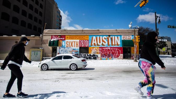Orang-orang yang berjalan sepanjang jalan yang tertutup salju di Austin, Texas. Badai Musim Dingin Uri telah membawa cuaca dingin bersejarah ke Texas, menyebabkan kemacetan lalu lintas dan pemadaman listrik. [Montinique Monroe / Getty Images / AFP]