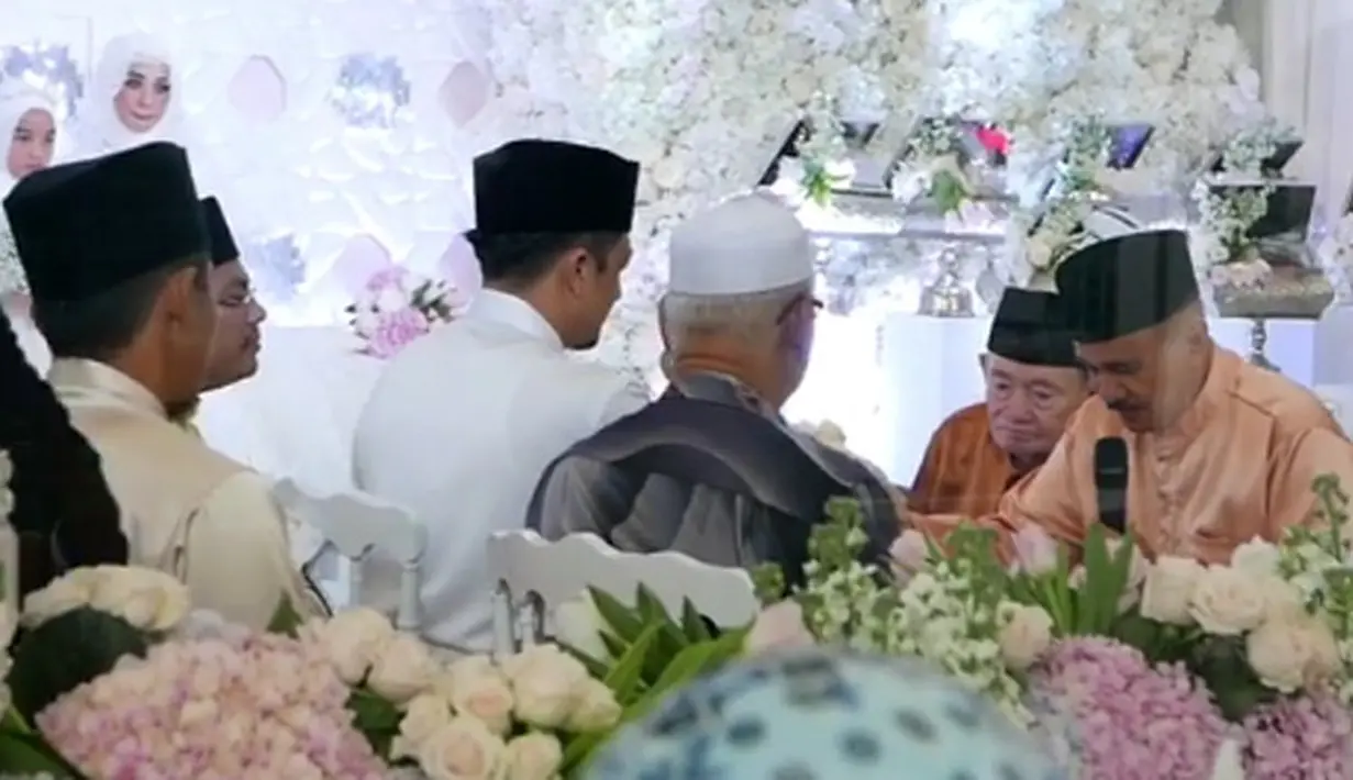 Bella nampak begitu cantik dengan balutan busana putih. Begitu juga mempelai pria, Engku Emran dengan balutan busana warna senada dengan peci warna hitam di kepalanya. (Instagram/noradanish)