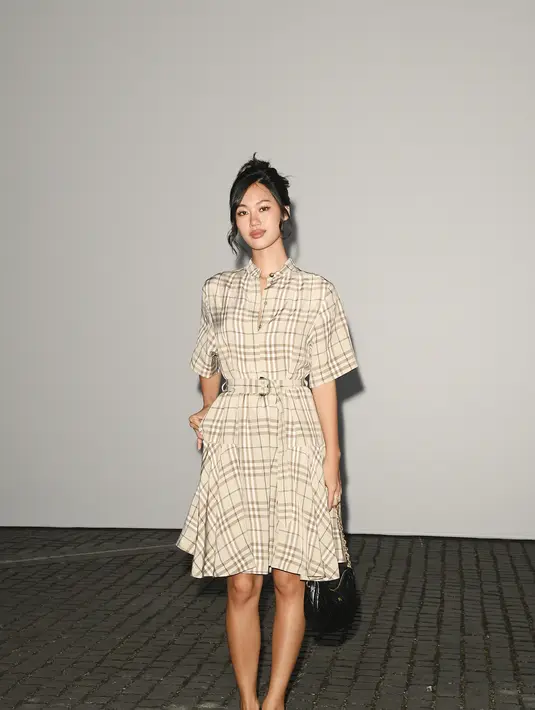 Jihoon Kim mengenakan dress kemeja pendek bermotif kotak-kotak krem khas Burberry, dilengkapi ikat pinggang senada, tas kulit kuilting hitam, dan pumps hitam. [dok. Burberry]