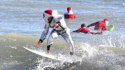 Peselancar Corey Howell yang menganakan pakaian luar angkasa serta Sinterklas berselancar untuk acara tahunan ke-14 Surfing Santas of Cocoa Beach di Cocoa Beach, Florida, Amerika Serikat, 24 Desember 2022. (Malcolm Denemark/Florida Today via AP)