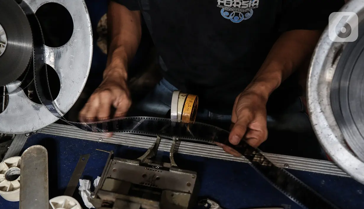 Adul (29) menyiapkan film seluloid 35mm untuk pertunjukan layar tancap di gudang rumahnya di Jakarta, Rabu (28/4/2021). Selama pandemi order penyewaan untuk layar tancap terjun bebas hingga menurun 90 persen. Pemberlakuan kebijakan selama Covid-19 sungguh sangat menampar usaha mereka. (Liputan6.com