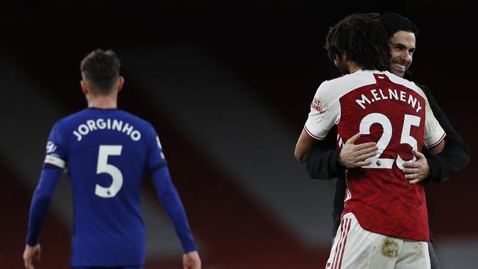 Pelatih Arsenal, Mikel Arteta tersenyum sambil memeluk gelendang Mohamed Elneny usai pertandingan melawan Chelsea pada lanjutan Liga Inggris di Stadion Emirates di London, Minggu (27/12/2020). Sebelum menang atas Chelsea, Arsenal sudah paceklik kemenangan di empat laga. (AFP/Pool/Adrian Dennis)