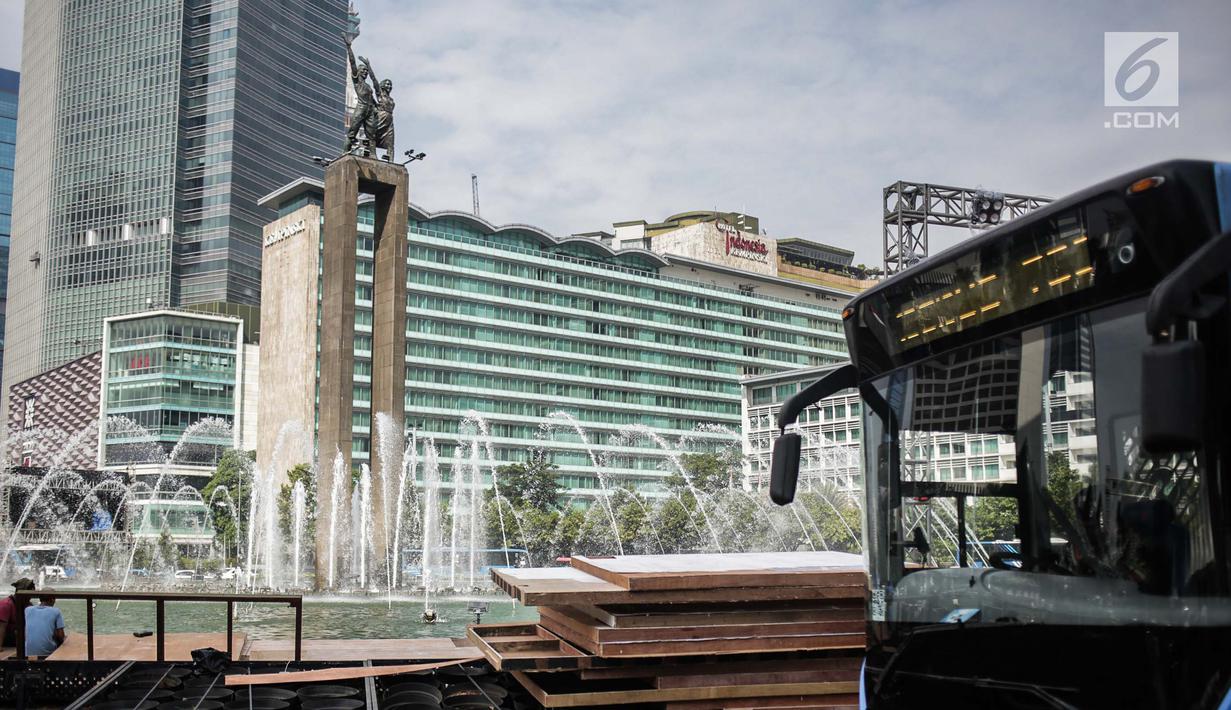 Bus Transjakarta melintas saat pekerja menyelesaikan pembuatan panggung HUT ke-492 DKI di area Bundaran HI, Jakarta, Kamis (20/6/2019). HUT ke-492 DKI akan dimeriahkan dengan acara Jakarta Night Festival dan Jakarta Creative Night. (Liputan6.com/Faizal Fanani)