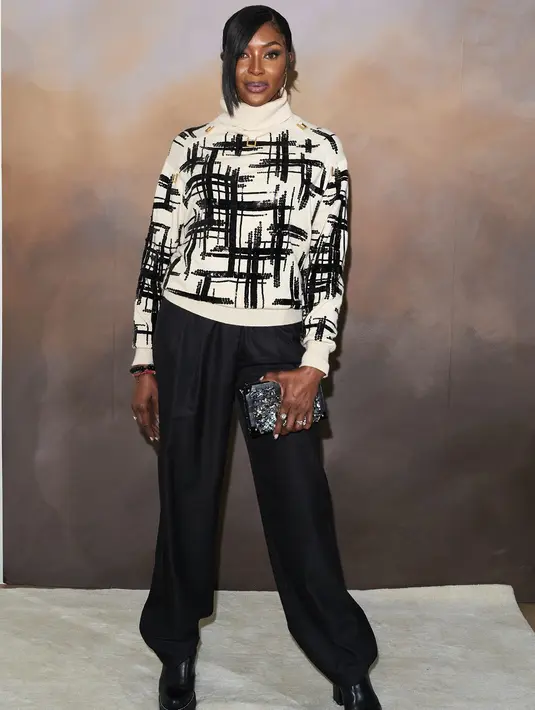Naomi Campbell tampil boyish dengan sweater turtleneck bercorak garis-garis abstrak, dipadu dengan celana panjang dan sepatu hitam. Foto: Document/Louis Vuitton.
