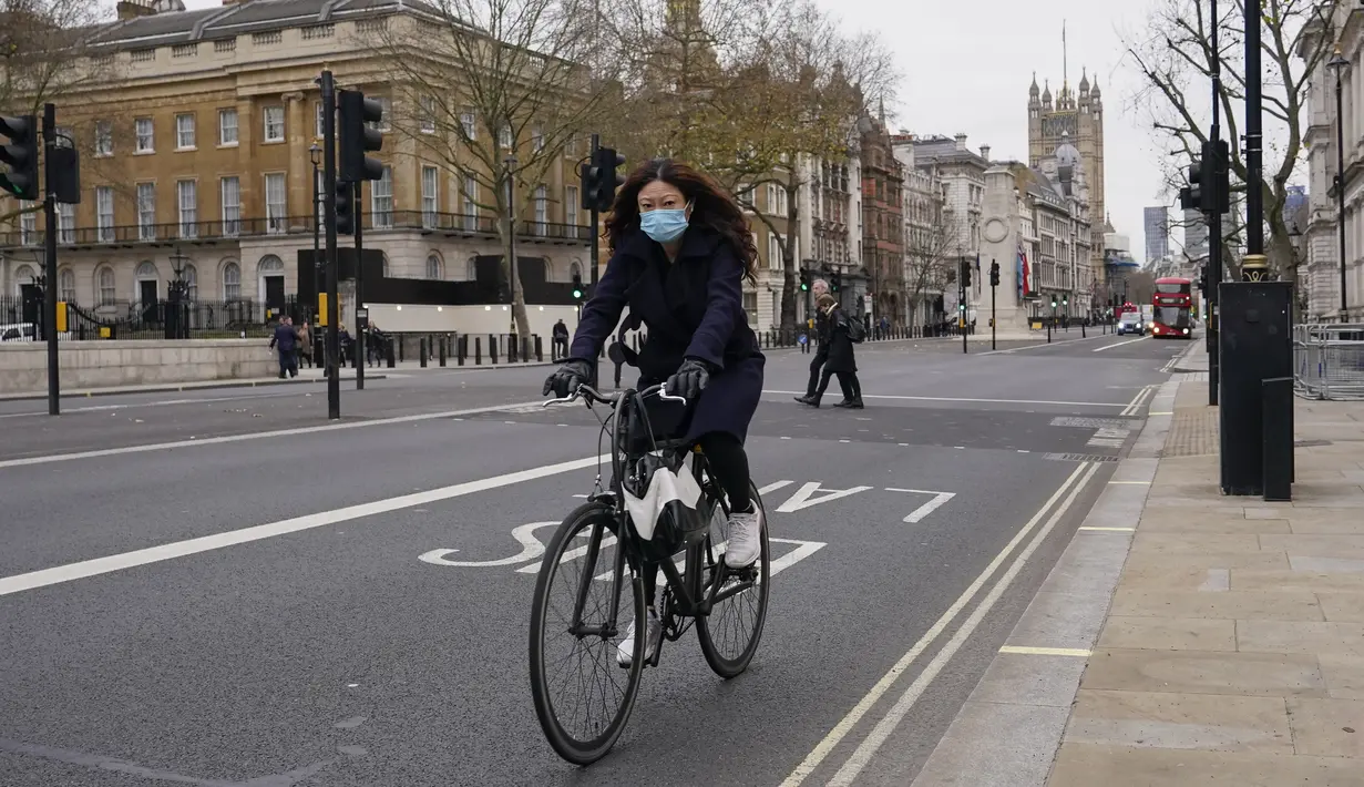 Seorang wanita mengenakan masker saat dia bersepeda di Westminster, di London, Kamis (16/12/2021). Inggris mencatat jumlah tertinggi infeksi COVID-19 baru yang dikonfirmasi pada hari Rabu (15/12) sejak pandemi dimulai. (AP Photo/Alberto Pezzali)