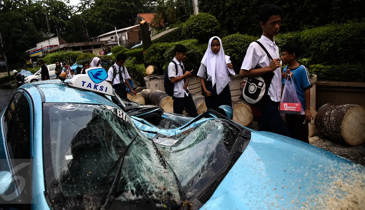 Sejumlah pelajar berjalan di dekat taksi yang ringsek tertimpa pohon tumbang di Jalan Taman Kebon Sirih, Jakarta, Selasa (30/8). Pohon itu tumbang akibat hujan deras disertai angin kencang yang melanda Jakarta tadi siang. (Liputan6.com/Faizal Fanani) 
