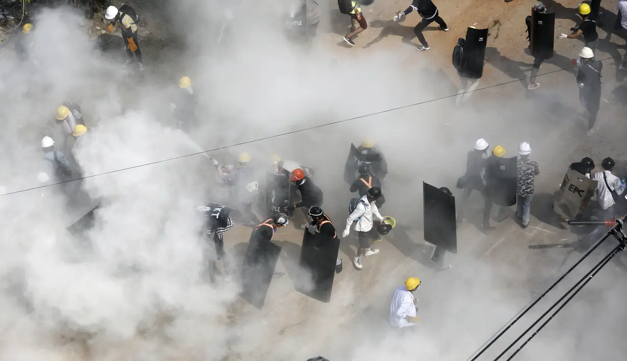Para pengunjuk rasa bereaksi ketika mereka diliputi oleh gas air mata yang ditembakkan oleh polisi, dan ketika pengunjuk rasa lainnya melepaskan alat pemadam kebakaran, selama demonstrasi menentang kudeta militer di Yangon (6/3/2021). (AFP Photo)