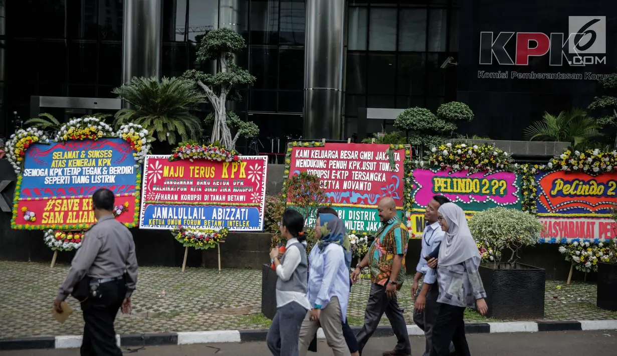 Warga melintas dekat karangan bunga berisi dukungan pada KPK di halaman Gedung KPK, Jakarta, Senin (20/11). Karangan bunga tersebut sebagai bentuk dukungan masyarakat kepada KPK terhadap pemberantasan kasus korupsi e-KTP. (Liputan6.com/Faizal Fanani)
