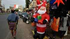 Warga berjalan melintasi balon Santa Claus dan barang hiasan Natal lainnya yang dipajang di toko pinggir jalan di Thiruvananthapuram, negara bagian Kerala, India, (19/12). Umat Kristen akan merayakan Hari Natal pada 25 Desember. (AP Photo / R S Iyer)