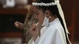 Seorang gadis makan wafer selama upacara Perjamuan Kudus pertama di tengah pandemi virus corona baru di gereja Katolik Nuestra Senora de la Merced di Lima, Peru, Jumat (3/12/2021). (AP Photo/Martin Mejia)