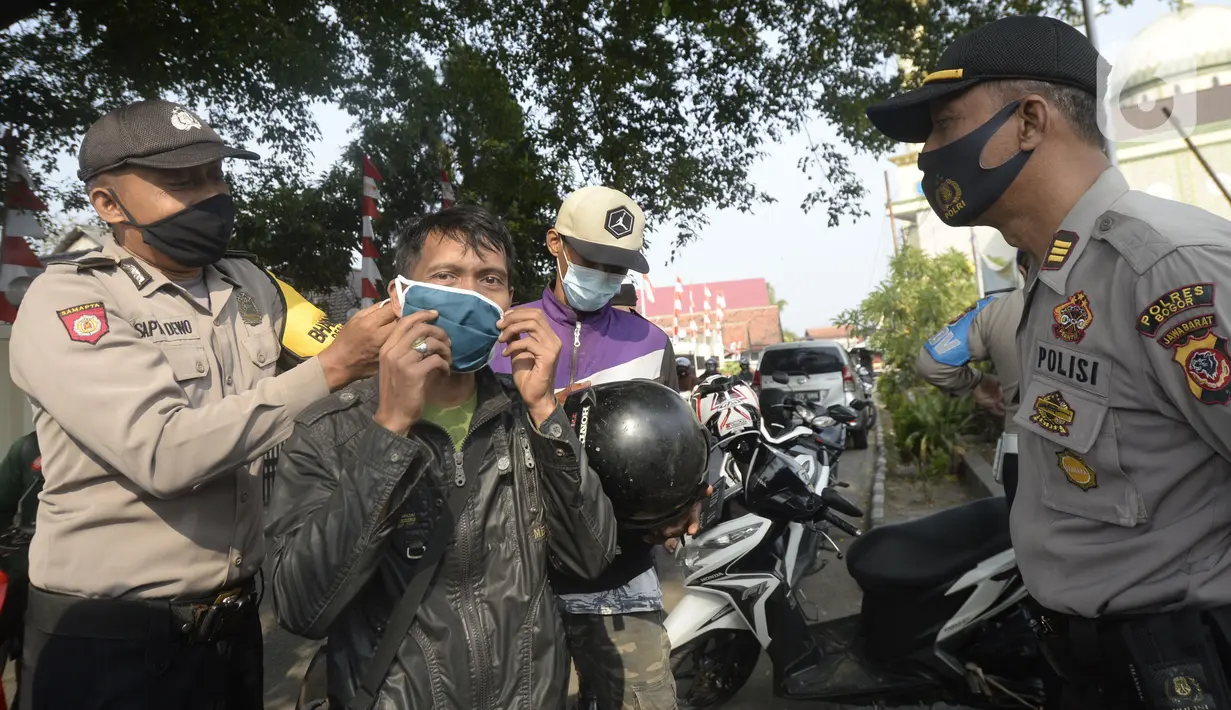 Anggota polisi dari Polsek Parung membantu memasangkan masker kepada pengendara sepeda motor di depan Polsek Parung, Kabupaten Bogor, Jawa Barat, Rabu (2/9/2020). Pembagian masker gratis setiap usai apel ini inisiatif anggota sejak masa pandemi COVID-19. (merdeka.com/Dwi Narwoko)