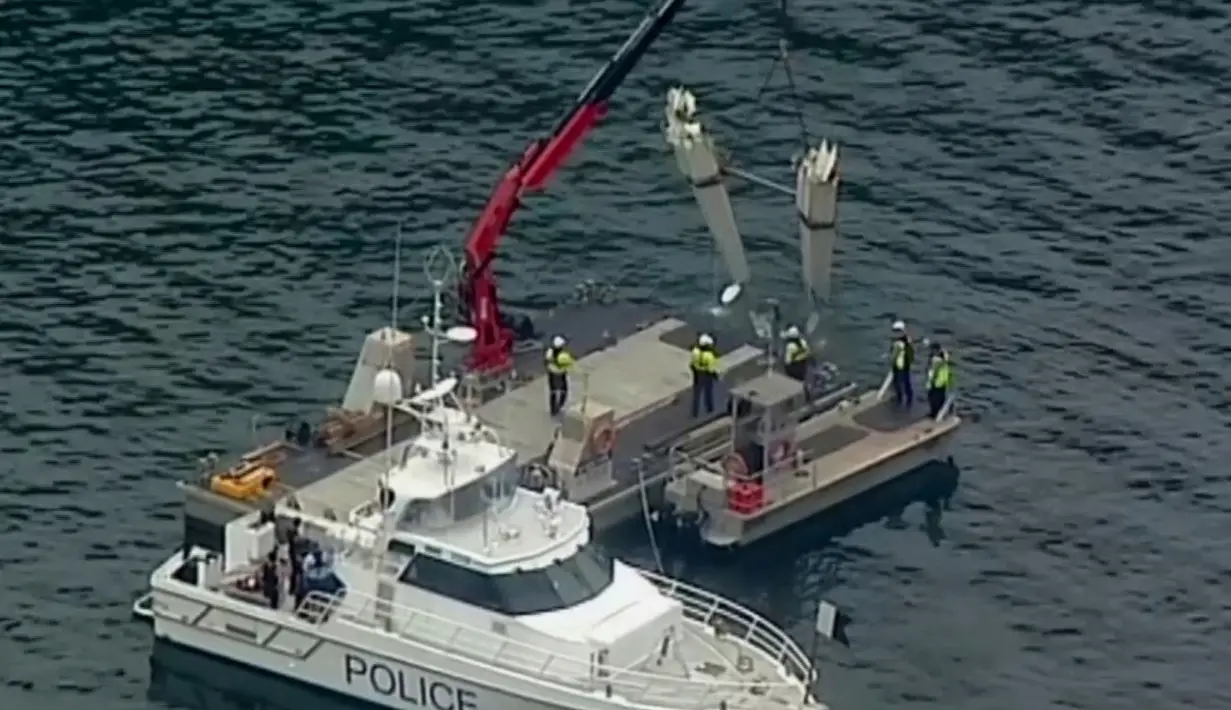 Petugas menggunakan derek dalam operasi pengangkatan bagian pesawat amfibi dari Sungai Hawkesbury, Sydney, Kamis (4/1). Bangkai kapal diangkat ke sebuah tongkang dan ditutupi dengan terpal karena sifat operasi yang sensitif (Mick Tsikas/AAP Images via AP)